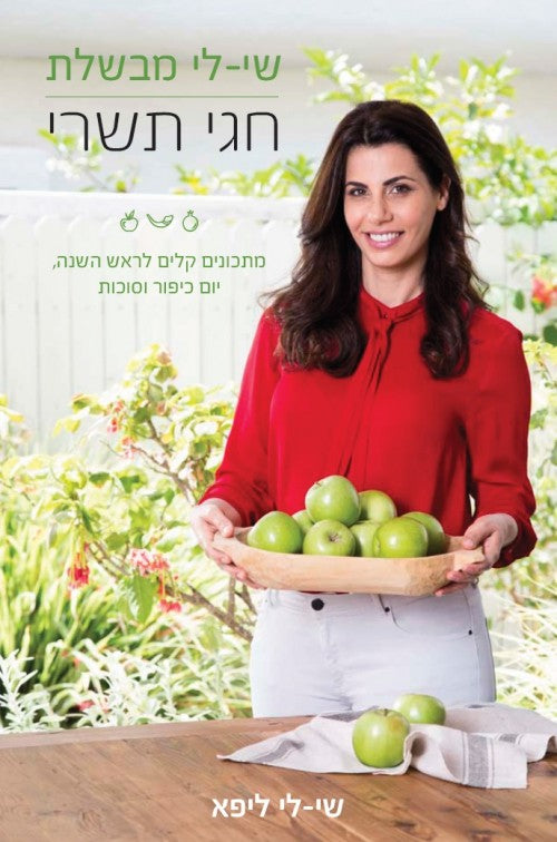 A cover of a Hebrew cookbook titled 'Shaliy Cooks - Tishrei Holidays - Shaily Lipa' featuring a photograph of a woman in a red shirt holding a tray of green apples.
